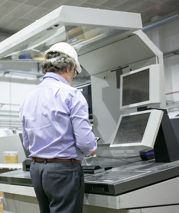 people, adult, man, male, caucasian, mature, grey hair, worker, employee, engineer, technician, professional, manager, hardhat, uniform, protective, helmet, indoors, glasses, shirt, operating, control, board, panel, monitor, using, tablet, digital, device, gadget, machine, technology, equipment, machinery, industrial, occupation, engineering, factory, industry, production, plant, work, manufacturing, job, labor, concept, portrait, back view, copy space, furniture, table, desk, person, belt